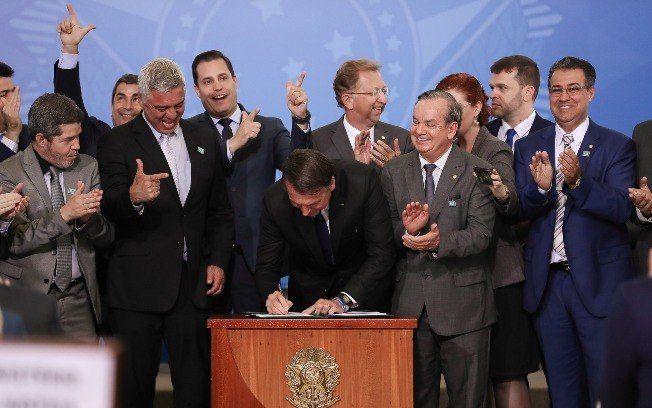 Bolsonaro, ovacionado por parlamentares da bancada da bala (que defendem interesses das indústrias de armas), assinando o Decreto